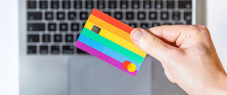 Hand showing a rainbow credit card in front of a laptop keyboard.