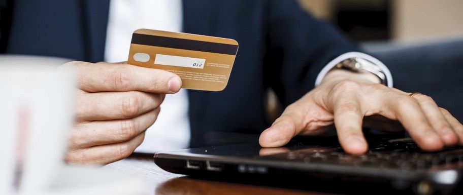 Man holding his credit card while typing on a laptop